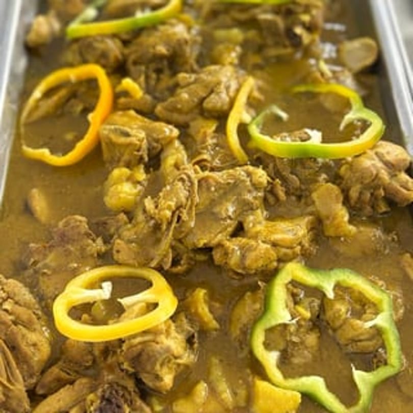Close-up of curry chicken with yellow and green bell pepper slices in a serving tray.