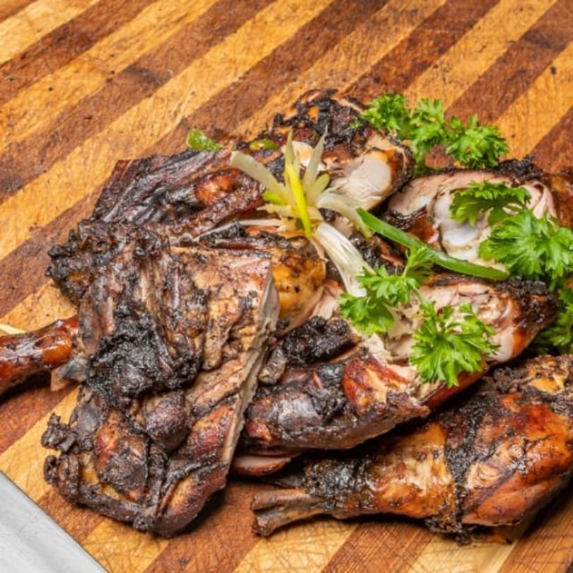 A platter of jerk chicken, garnished with fresh parsley and sliced scallions, on a wooden cutting board.