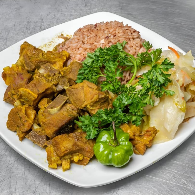 Curried goat with rice and peas, steamed cabbage, and a green scotch bonnet pepper.