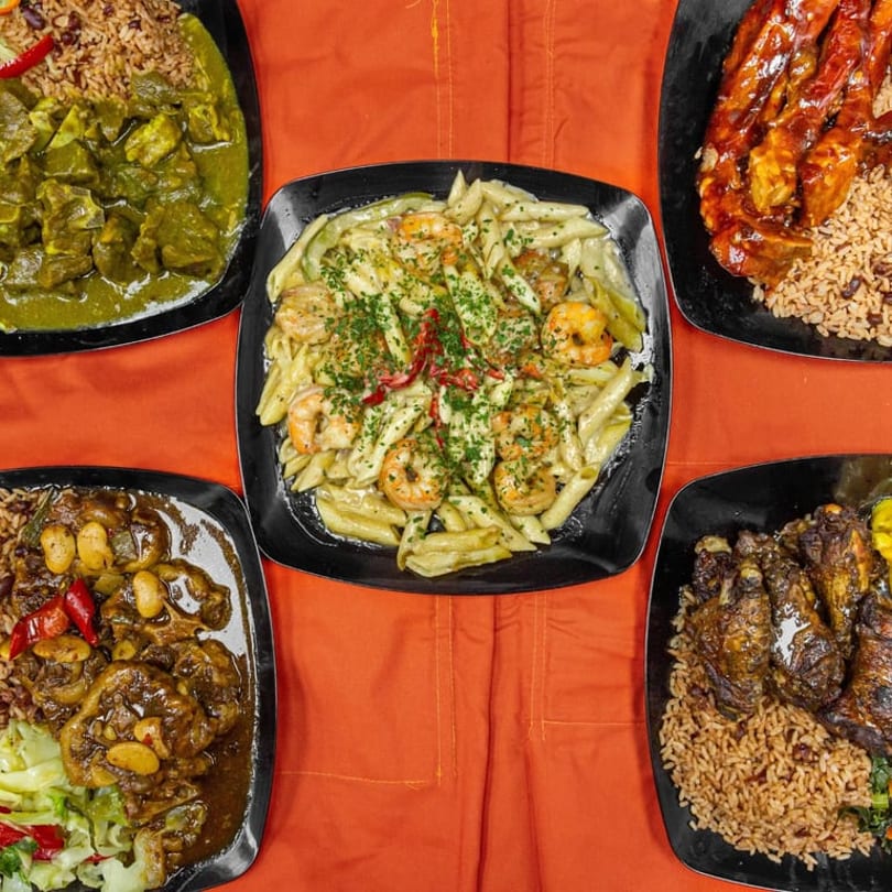 Five plates of diverse Caribbean dishes, including curry, pasta with shrimp, oxtail, and jerk chicken.