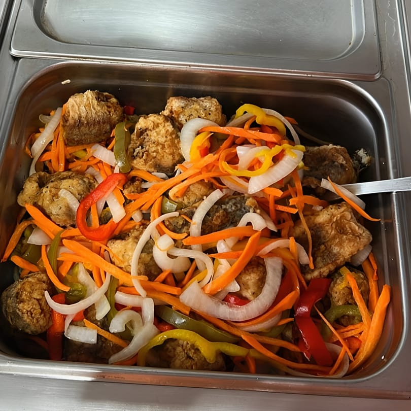Fried fish pieces mixed with colorful julienned carrots, onions, and bell peppers in a metal serving tray.