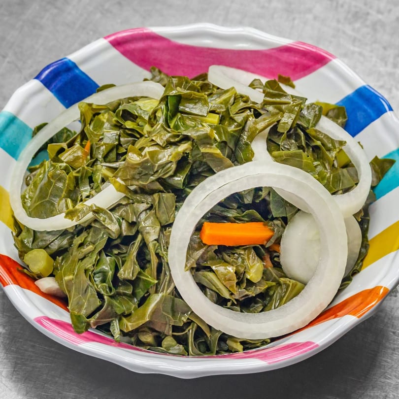 A colorful bowl of Jamaican collard greens with sliced onions and carrots.