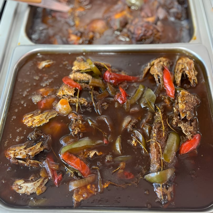 Close-up of Jamaican brown stew fish with peppers and onions in a buffet tray.