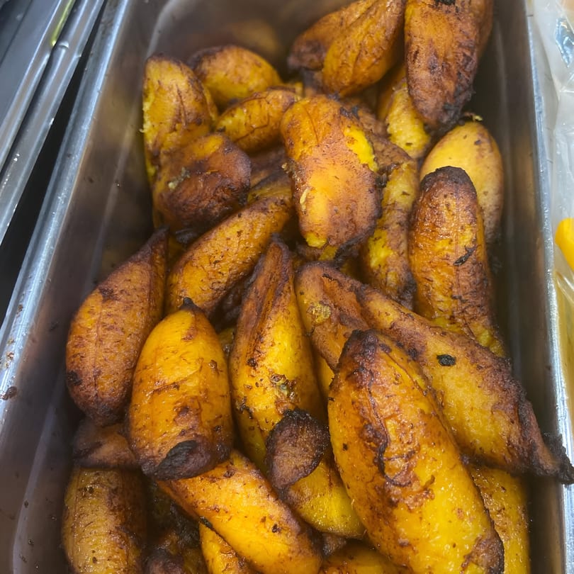 Close-up of a metal tray filled with golden-brown, caramelized fried plantains, a Jamaican specialty.