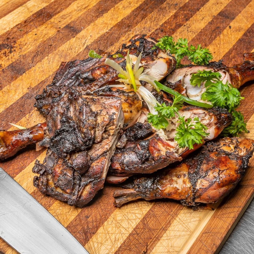 Close-up of Jamaican jerk chicken pieces, garnished with fresh parsley and scallions on a wooden cutting board.