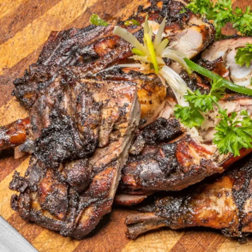 Close-up of Jamaican jerk chicken pieces, garnished with fresh parsley and scallions on a wooden board.